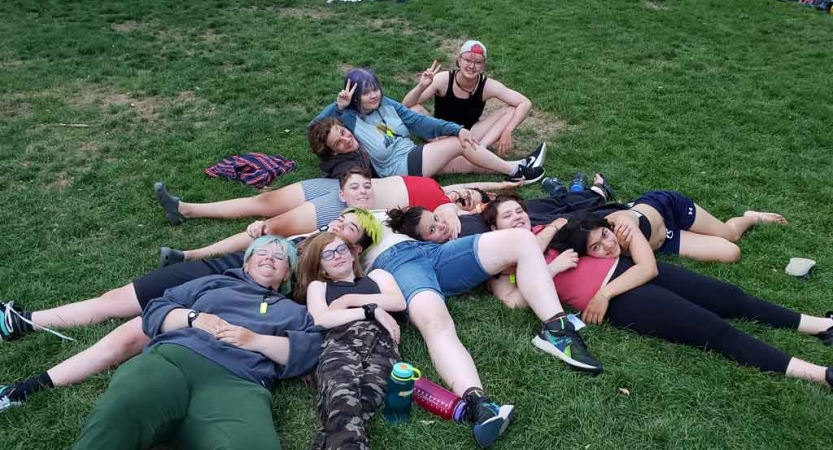 a group of students lay in a pile on grass during an outward bound trip for lgbtq+ teens